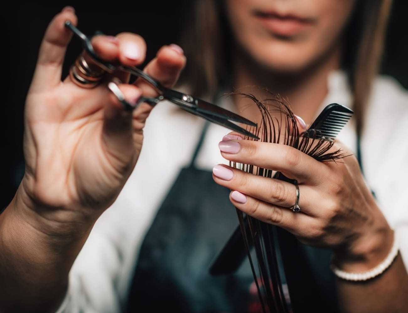 Hairdresser trimming hair with scissors and comb, close-up on hands in action.
